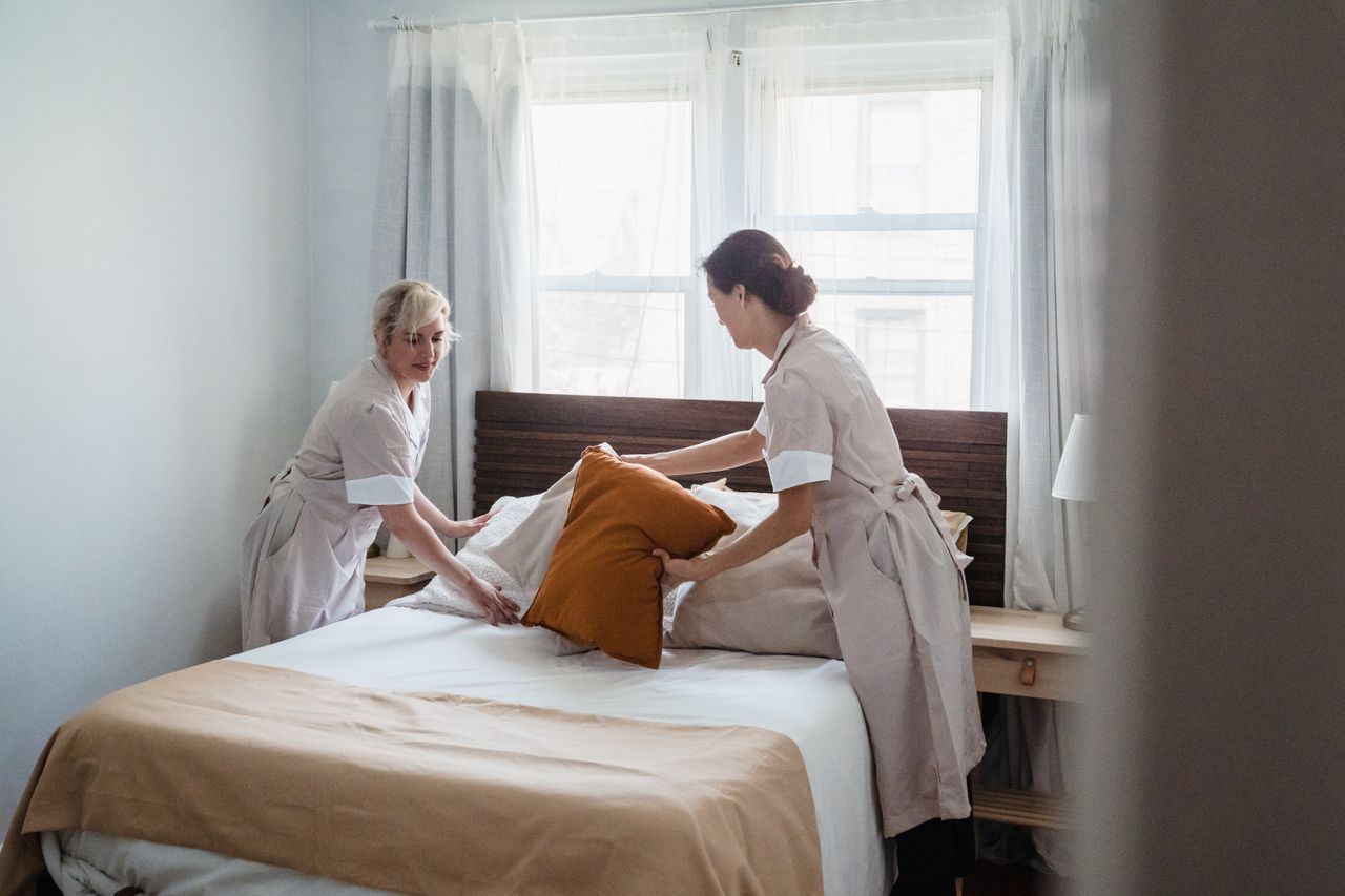 creative Two housekeepers organizing bed linen in a bright, cozy bedroom.